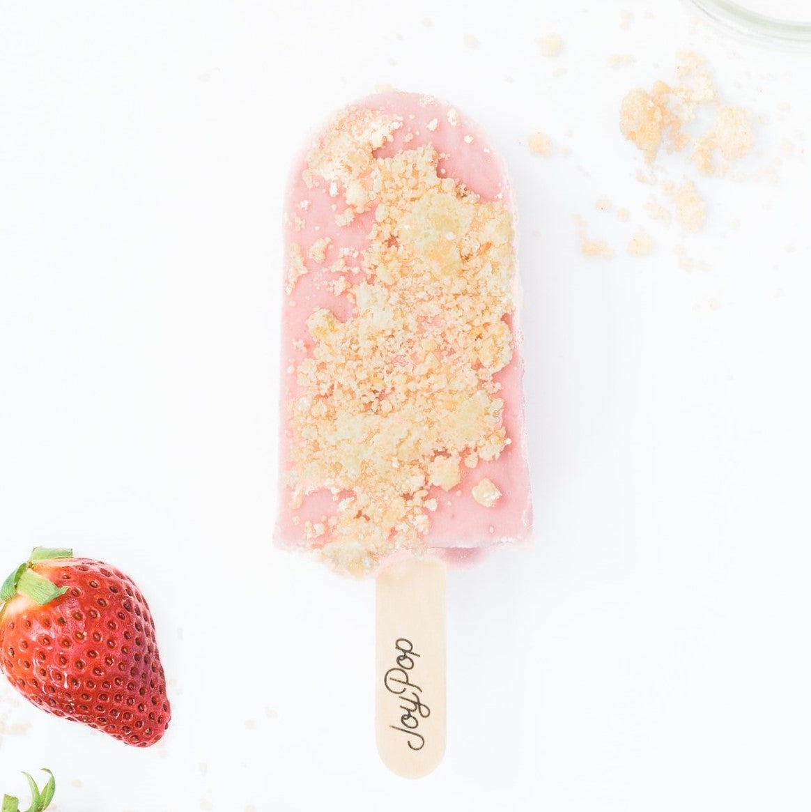 strawberries and cream frozen pop from The Joy Pop Co with fresh strawberries and shortbread crumble and a glass of milk on a white background