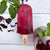 Hibiscus Mint Frozen Pop by The Joy Pop Co next to mint leaves and hibiscus leaves and a glass of hibiscus tea with a mint sprig on a white wood background