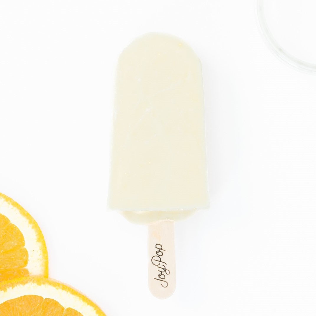 Orange cream frozen pop from The JoyPop Co on a white background with slices of orange on the sides
