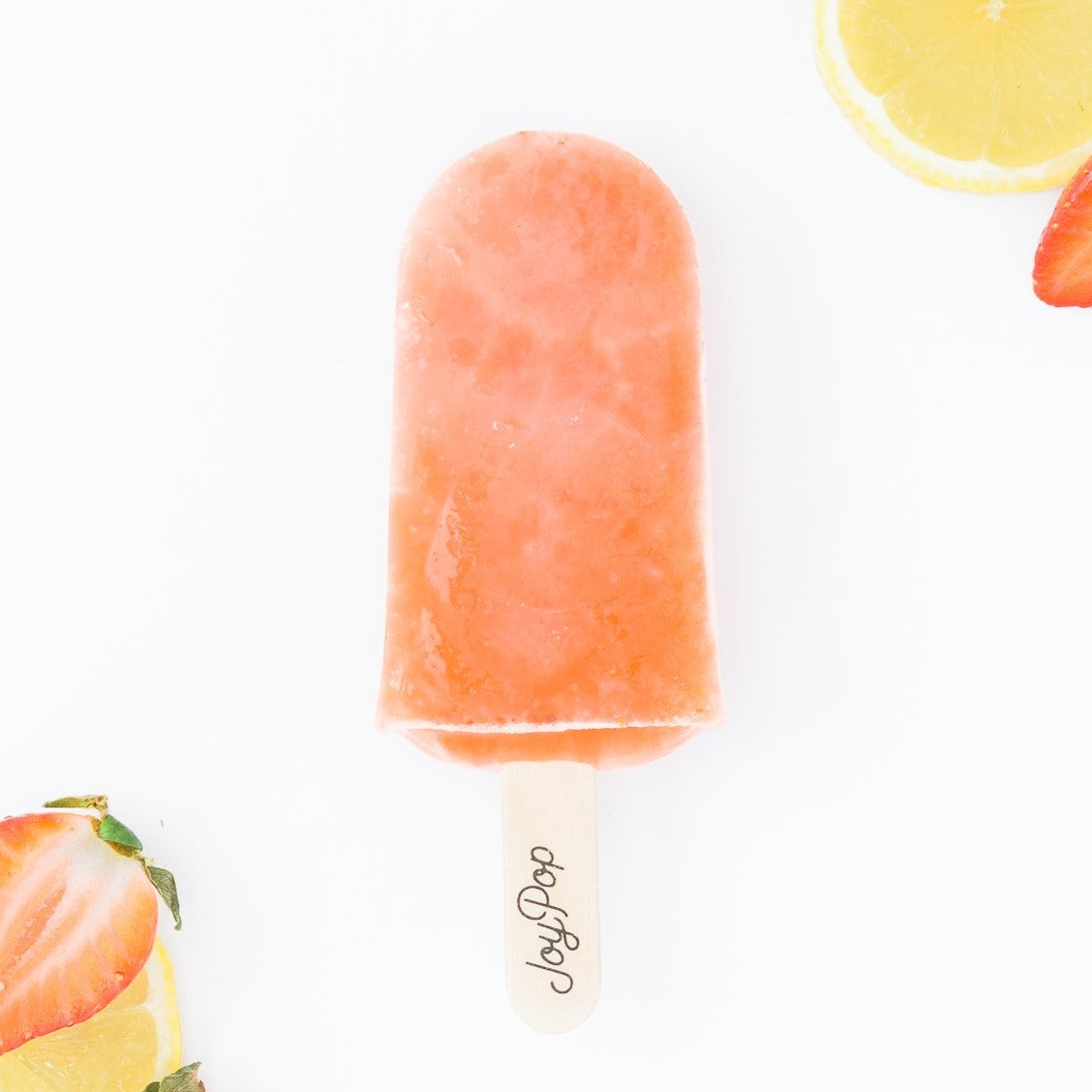 Strawberry Lemonade frozen pop from The Joy Pop Co with fresh strawberries and lemon slices on a white background